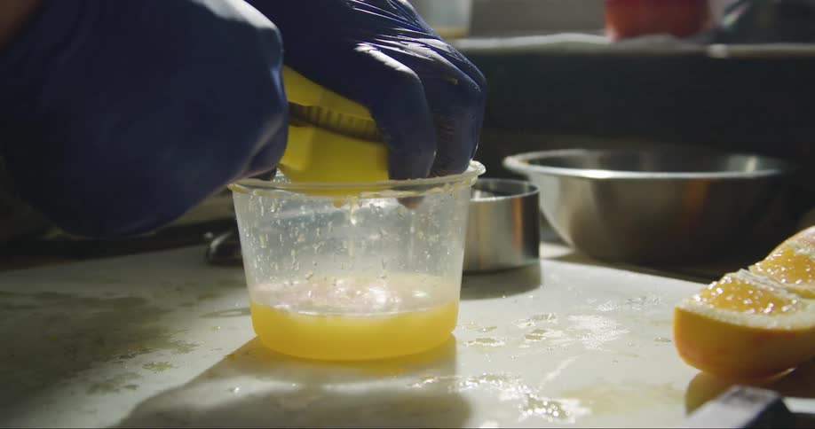 Person with purple gloves makes orange juice using hand juicer