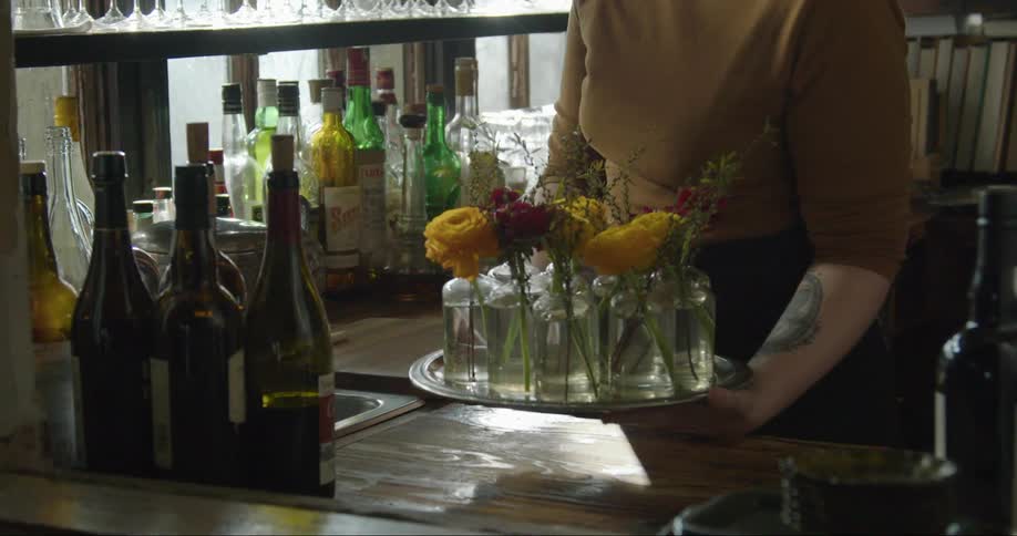 A woman places a tray of flower vases on a bar counter