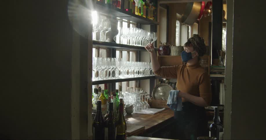 A restaurant worker cleans a glass and holds it up to the light