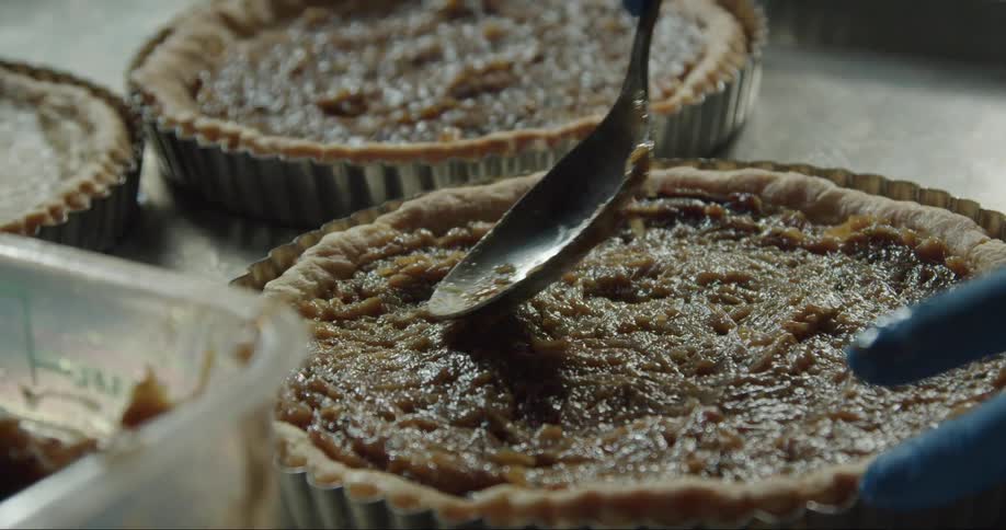 Baker spreads filling in one of several pies while wearing gloves