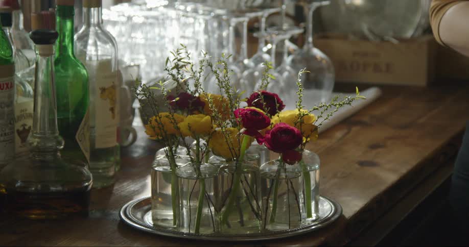 A woman sets up flowers by the wine glasses