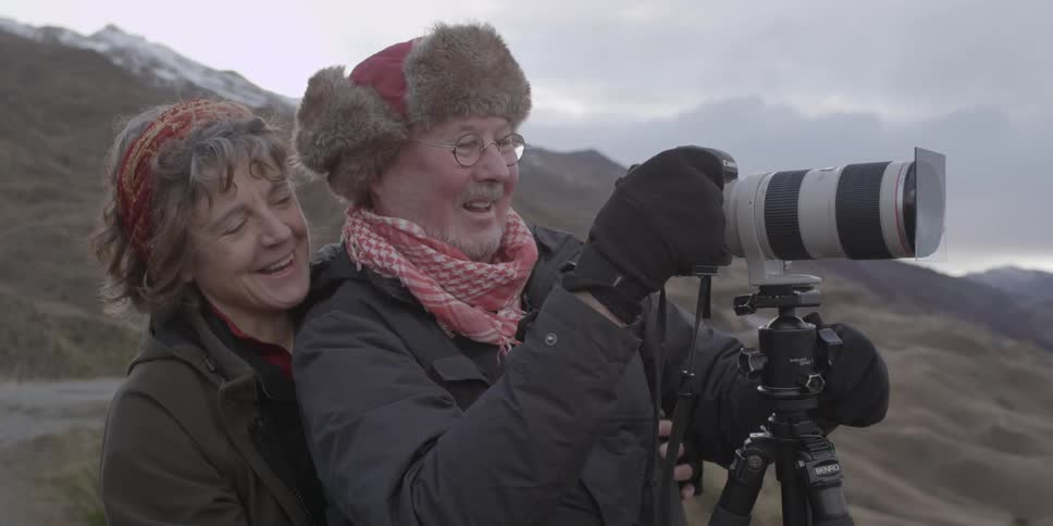 A woman hugs a man adjusting a camera