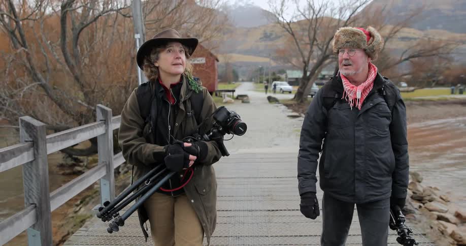 A man and woman walking across a bridge carrying cameras