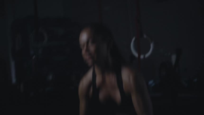 A woman in a dimly lit gym repeatedly lifts a weighted bag over her shoulder