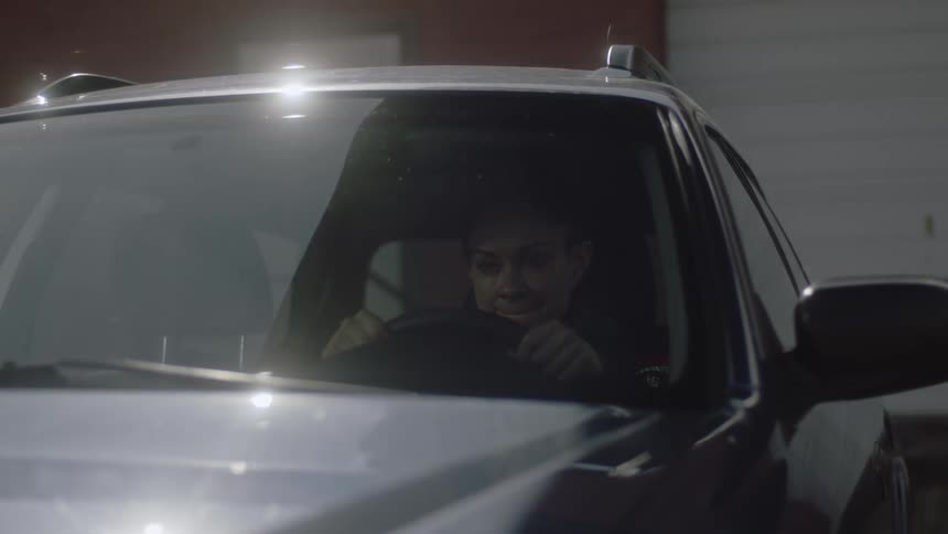 Sad woman sits in car in the garage