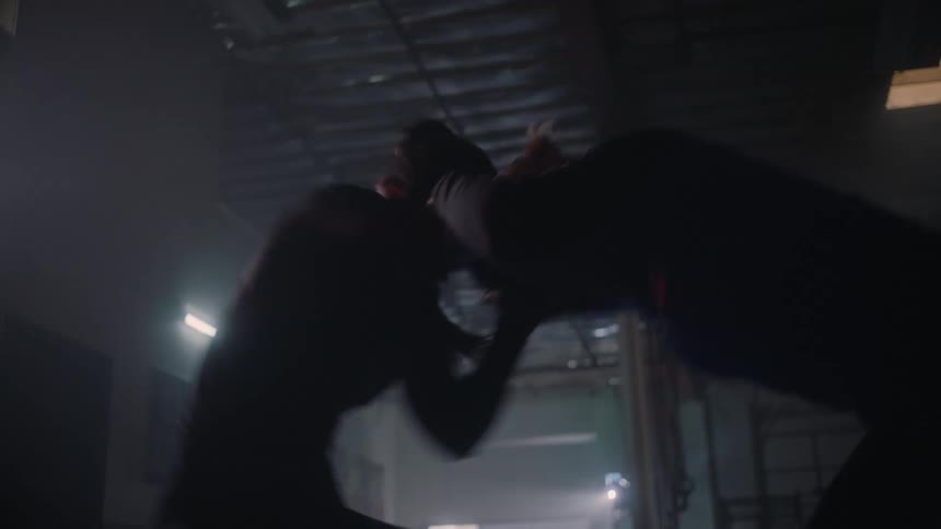 Two women wrestling each other in a dark space as they roll on the floor