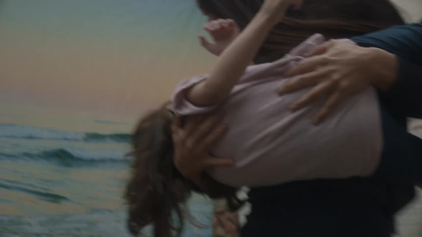 Mother plays with her daughter near clothesline holding sheet showing ocean scene