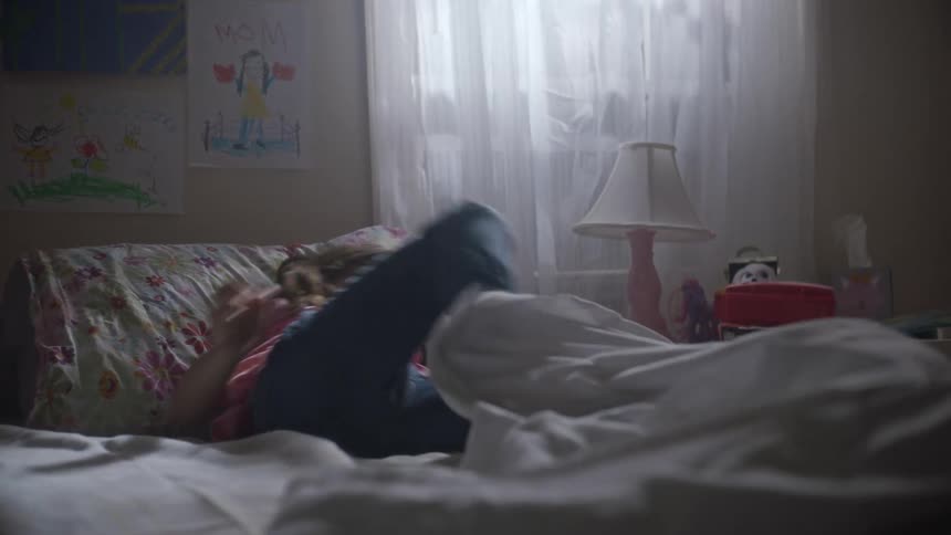 A young girl happily plays on the bed as someone else tosses a sheet over her
