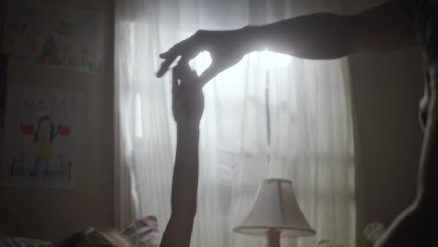 A young girl laying in her bed playing with her father sitting next to her