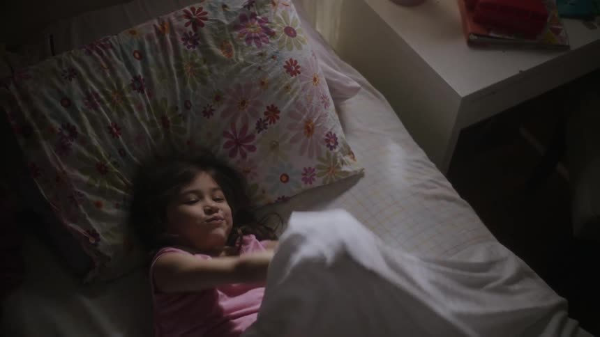 A girl raises her arms up as a bed sheet falls over her