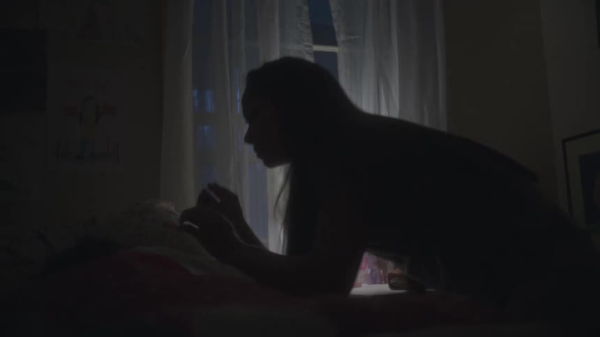 A mom turns on a bedside lamp and kisses her sleeping child
