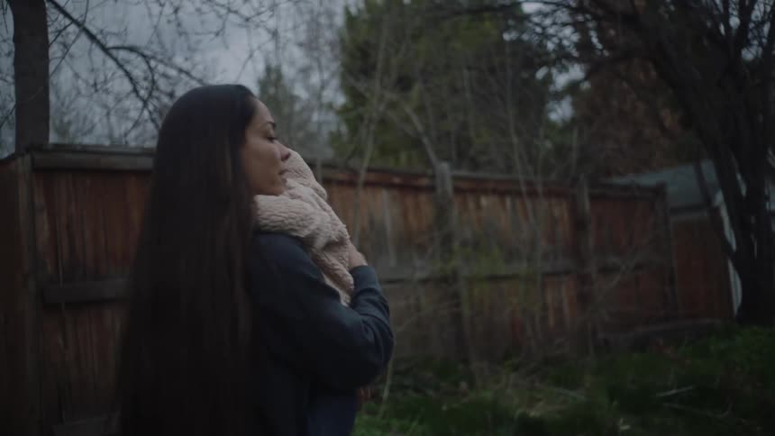Mother with dark straight hair and jacket gets out of car and carries his daughter in her arms