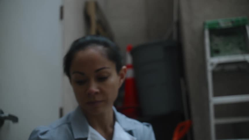 A woman is kneeling in a room with a mop bucket and ladder and she stands up and turns her head from side to side and dances
