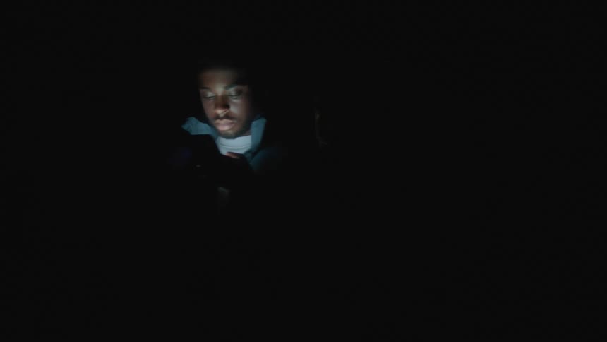 A man and woman standing back to back both looking down at their cell phones in a dark room as they spin around
