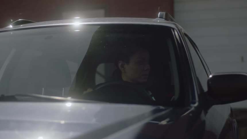 An anxious woman is sitting at the wheel of a car when a man knocks at the window and talks to her