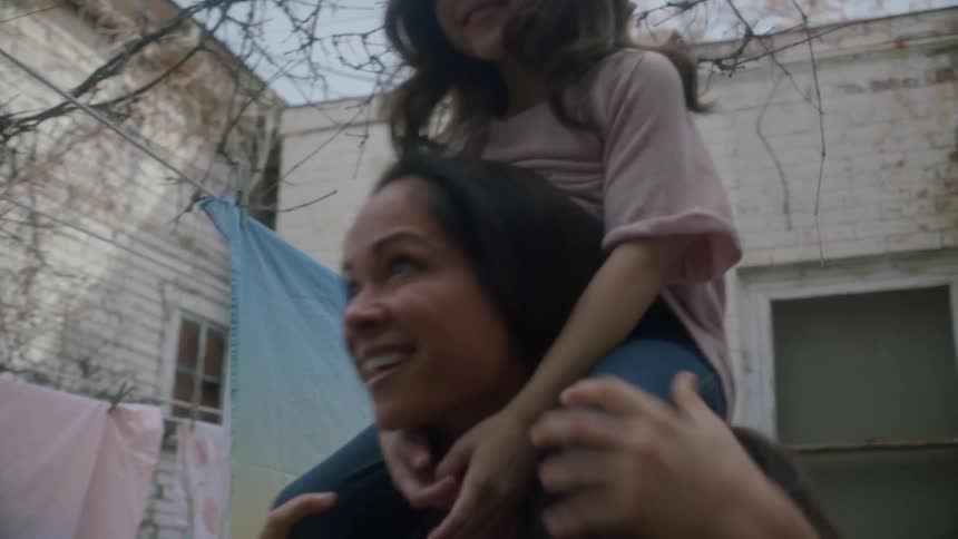 Mother carries daughter on her shoulders laughing in the backyard