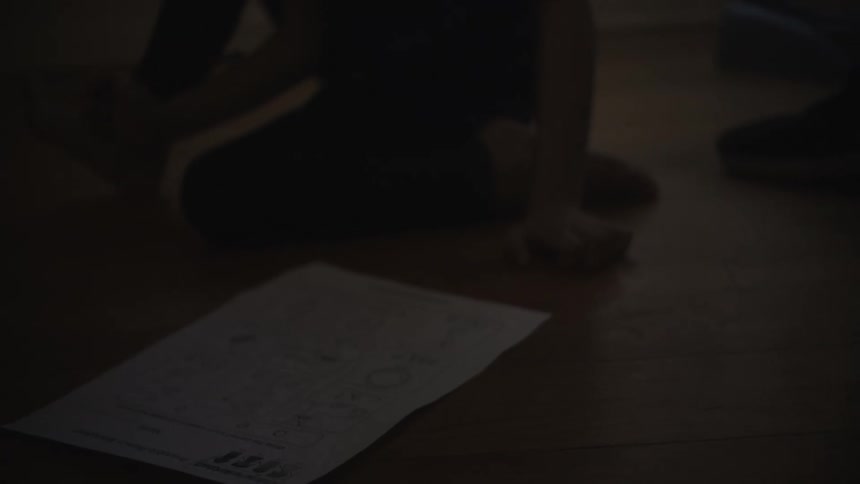 Mother helps daughter with her homework as girl sits on wooden floor
