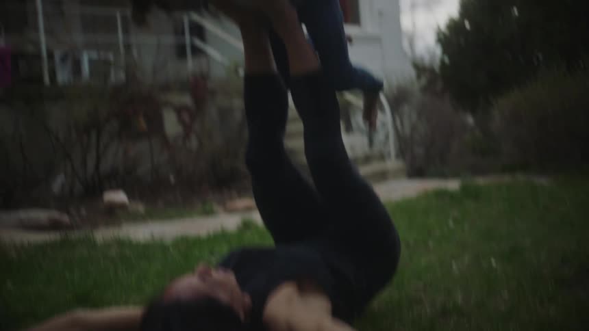 A woman lifts her daughter up with her legs while playing outside