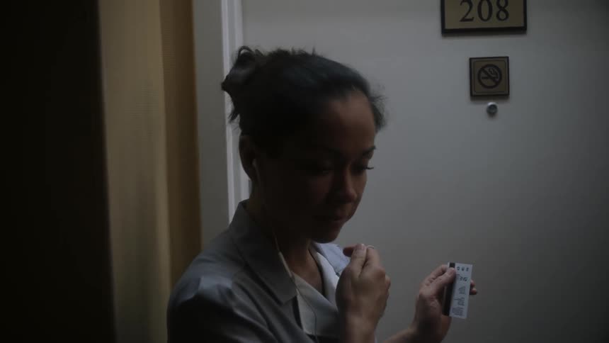 A female maid knocks on a door before removing her wired earbuds