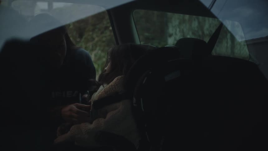 A woman wakes her sleeping daughter in the back of the car
