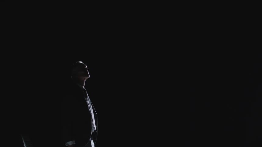 Man sitting in a dark area highlighted by light stands and looks around