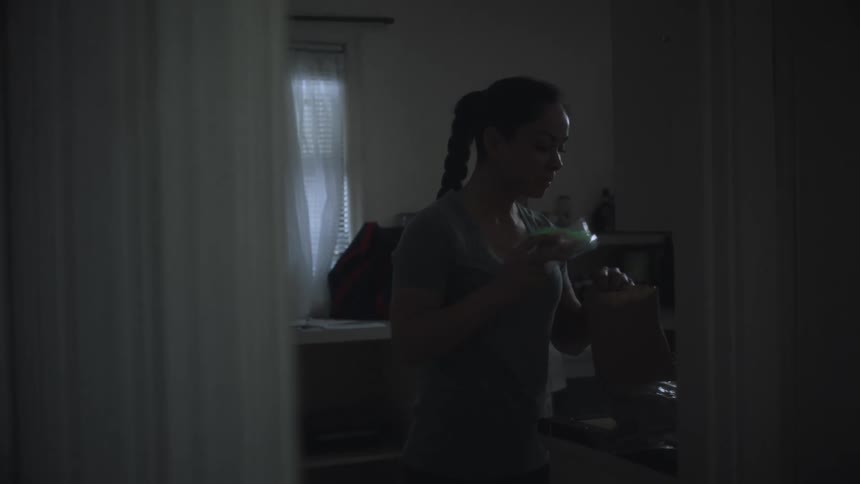 A woman standing in her kitchen placing food into a baggie and placing it in a paper bag