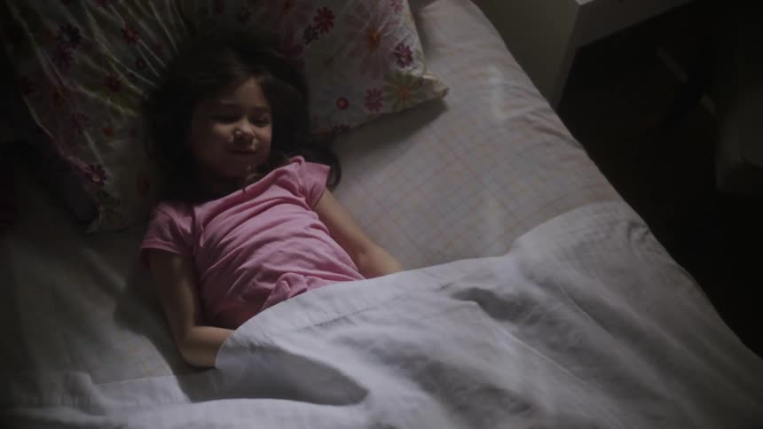 A little girl is lying on her bed as a sheet falls over her and lifts back up