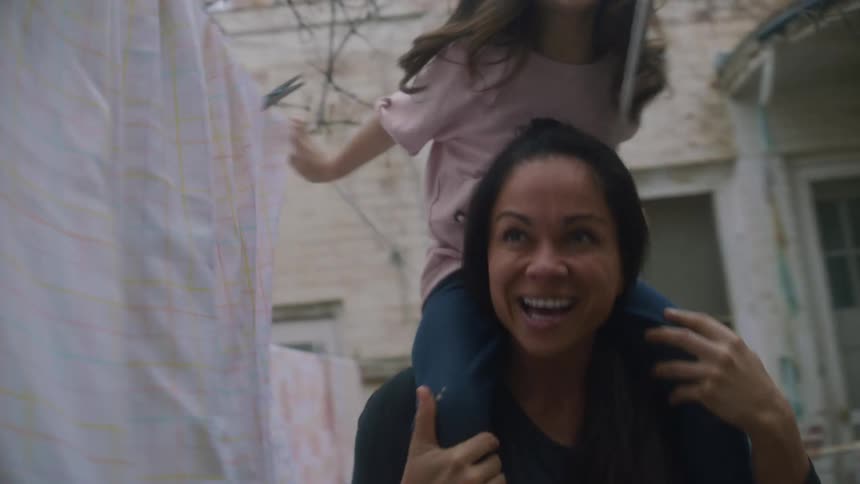 Mother carries daughter on her shoulders through clotheslines in the backyard