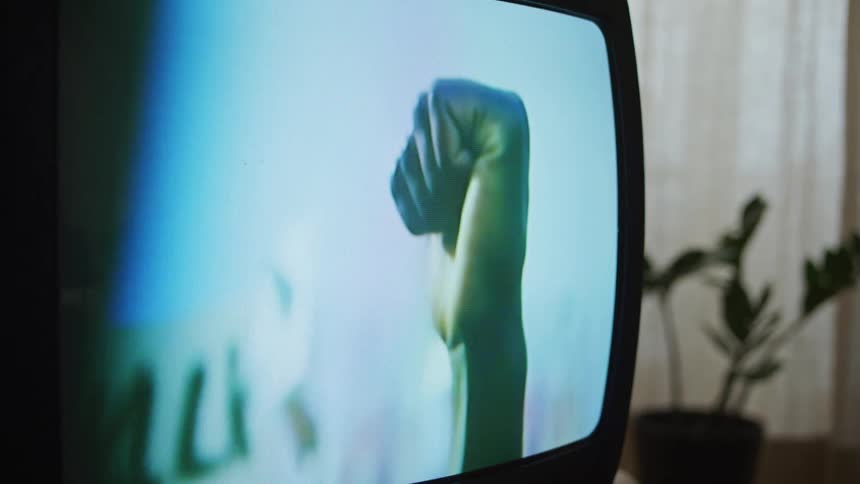 A close up of an old television screen with a persons hand in a fist on the screen