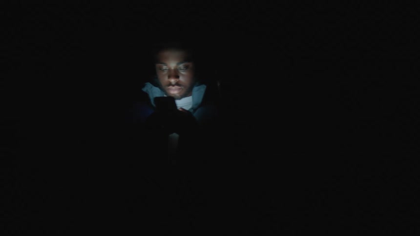 Teen boy and teen girl in the dark with only smartphone lighting up face rotating on a platform back to back both looking at their phones as they rotate