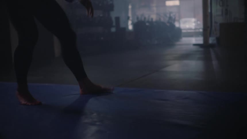 A woman in a dark gym doing squats on a mat and shadow boxing