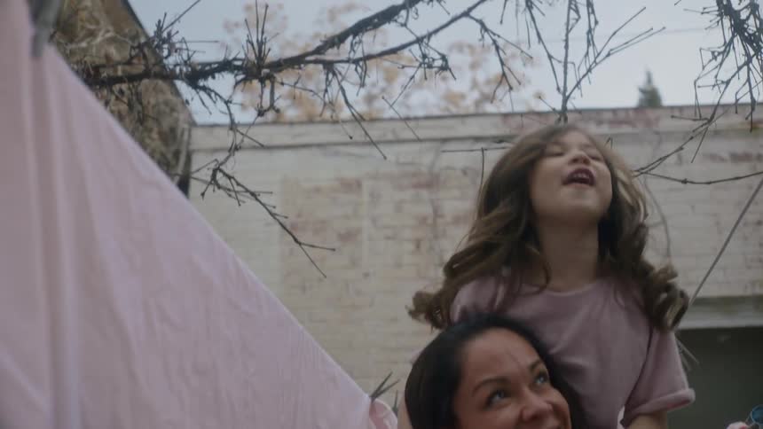 A woman carries her daughter on her shoulders while checking on laundry hanging outside