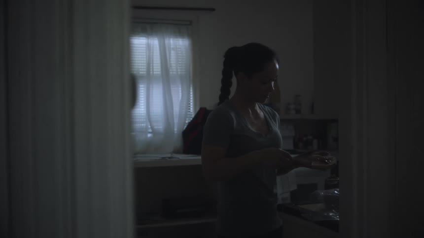 Woman with ponytail and gray shirt spreads jam on bread in the kitchen