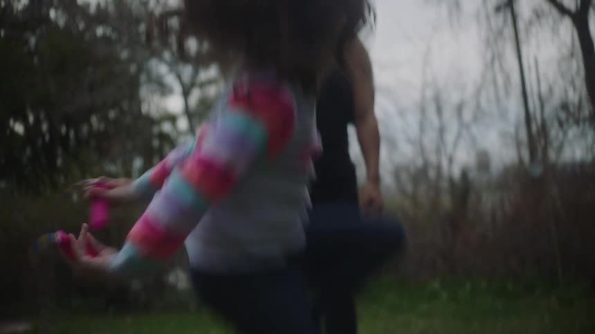 A little girl is playing in her yard with a jump rope as he mother stands watching and smiling
