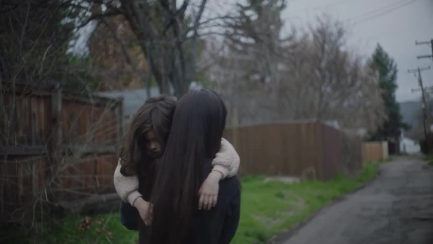 A woman is carrying a little girl as she walks on a neighborhood sidewalk near a fence