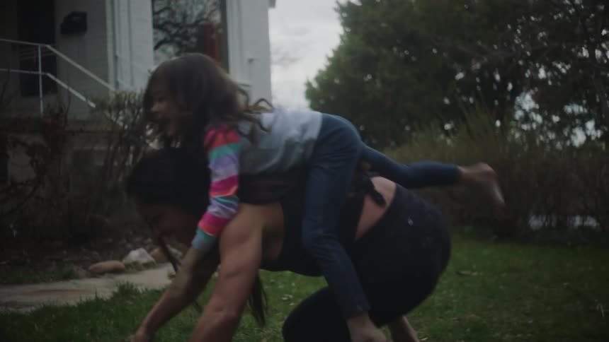 A muscular woman playfully allows her daughter to climb on her back