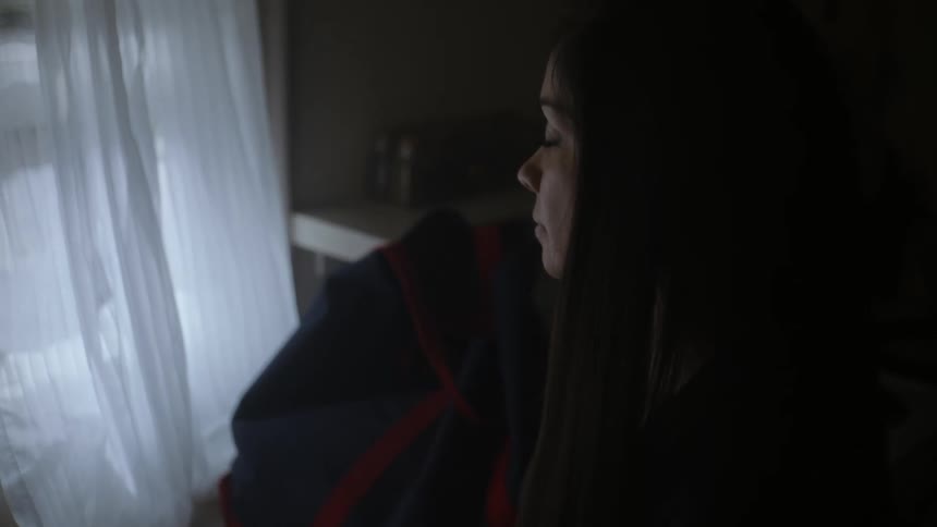 A woman sitting at a desk holding papers in her hands then looking out the window in front of her