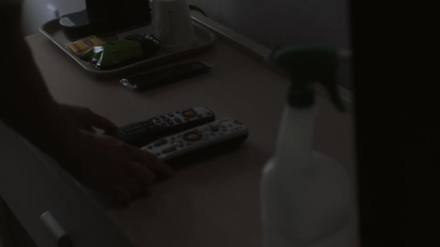 A hotel cleaner places remote controls on a dresser