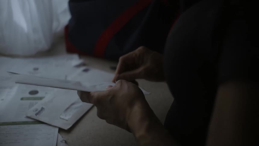 A woman sitting at a table picks up one of the letters scattered in front of her and opens it