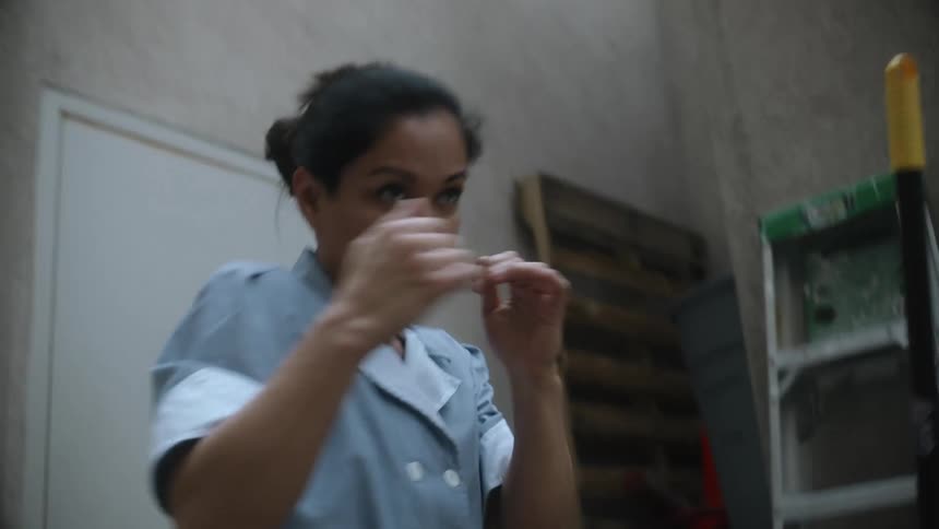 A woman dressed in a maids uniform practices boxing in a supply area at work