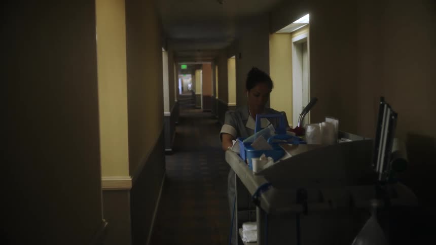 A hotel cleaning lady pushes her card down a corridor