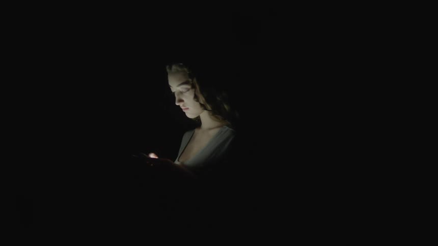 A woman looks down at her brightly lit phone