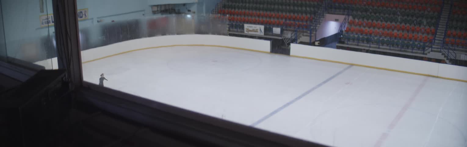 A woman skating in an ice rink is watched from a window above