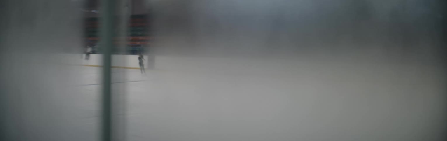 A person ice skates behind frosted glass in an indoor rink