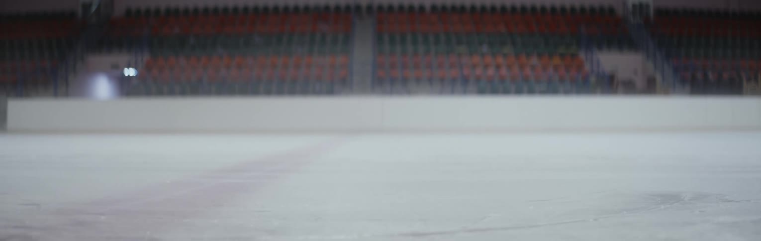 A person skating on an indoor ice rink doing spins along the back wall