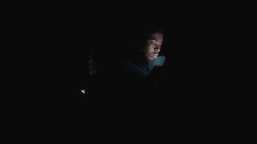 The faces of a young man and woman are illuminated by their smart phones