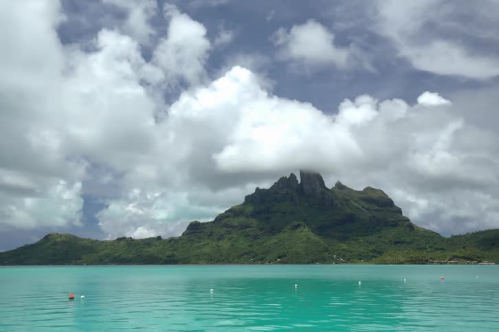 Clouds and a boat move by a mountain across the water