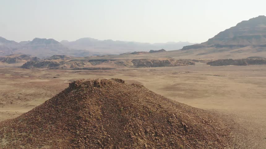 Dirt is piled in a tall mound in a dirt field below a canyon