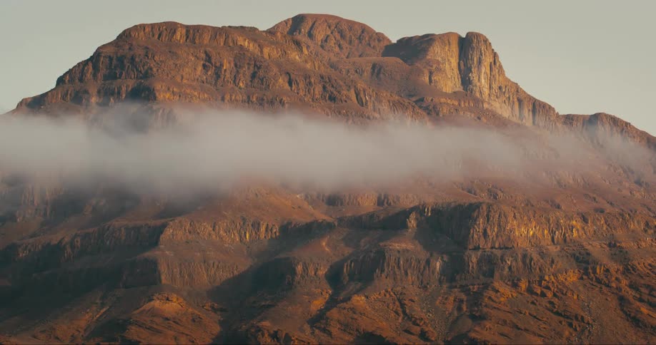 A thin gray cloud drifts in front of a brown rocky mountain