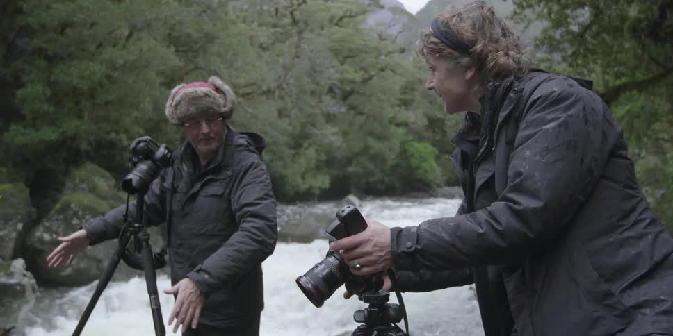 A man and woman set up their cameras near a stream